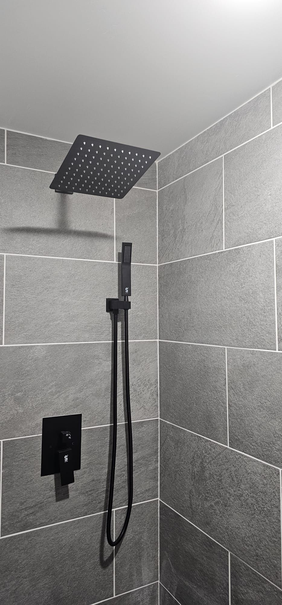 There is a black shower head in the corner of the shower.