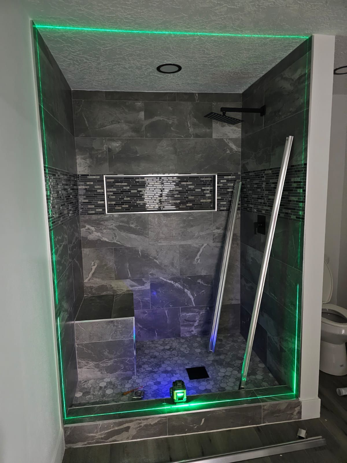A bathroom with a walk in shower with green lights.