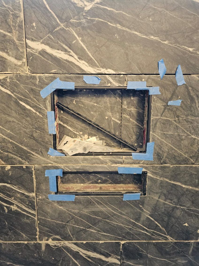 A marble wall with a hole in it and blue tape on it.