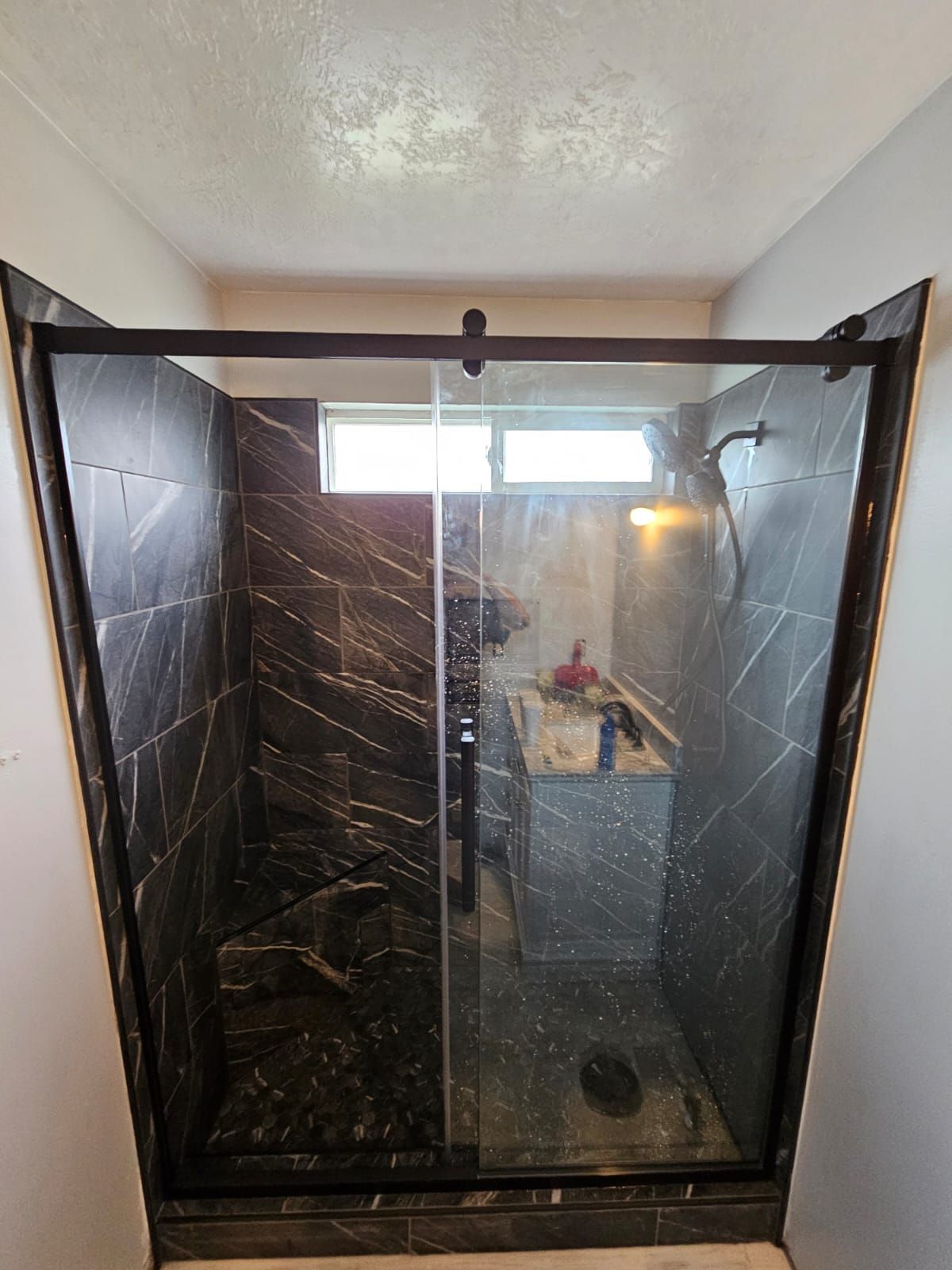 A bathroom with a sliding glass shower door and a window.