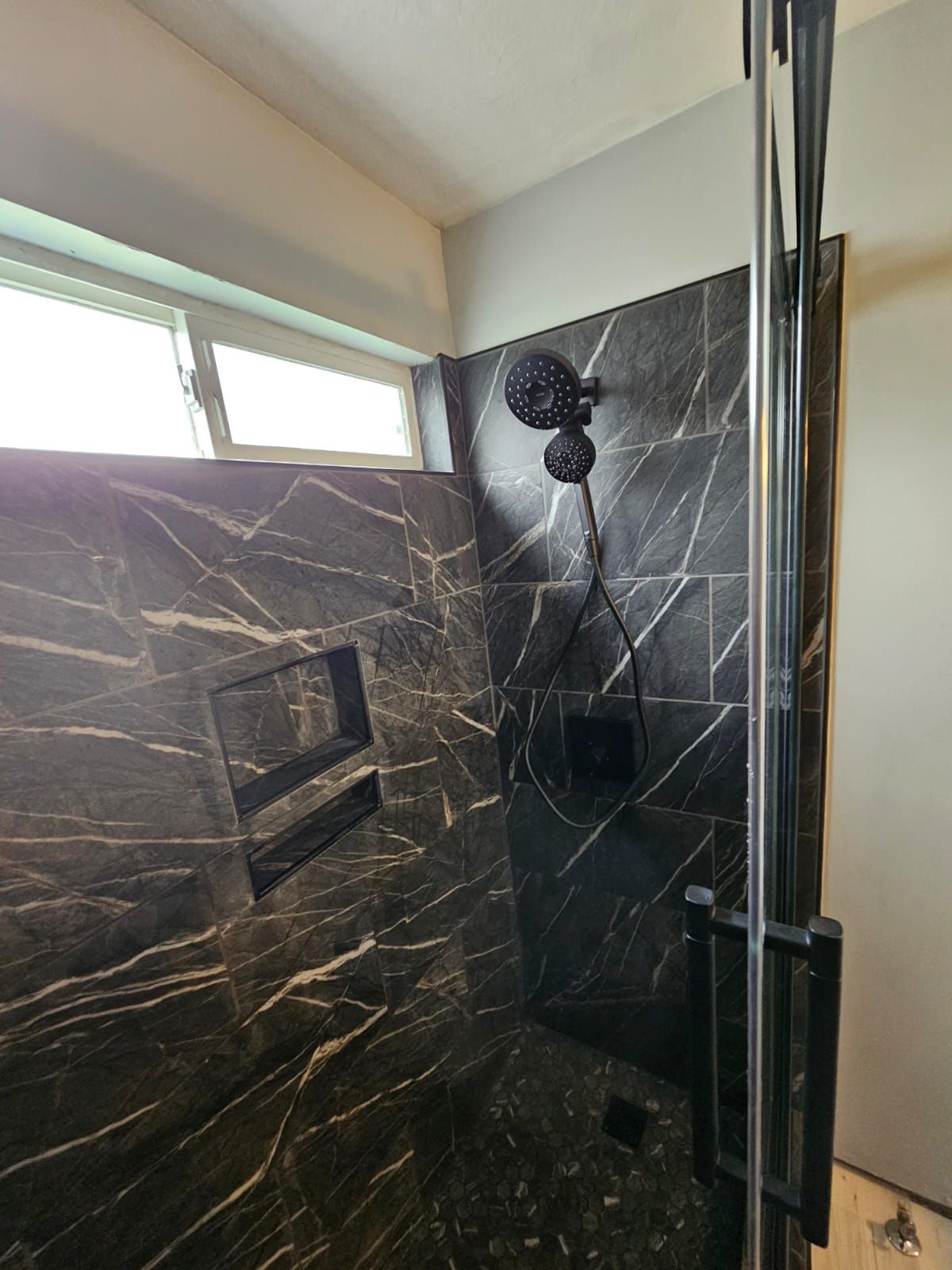 A shower with a black marble wall and a black shower head.