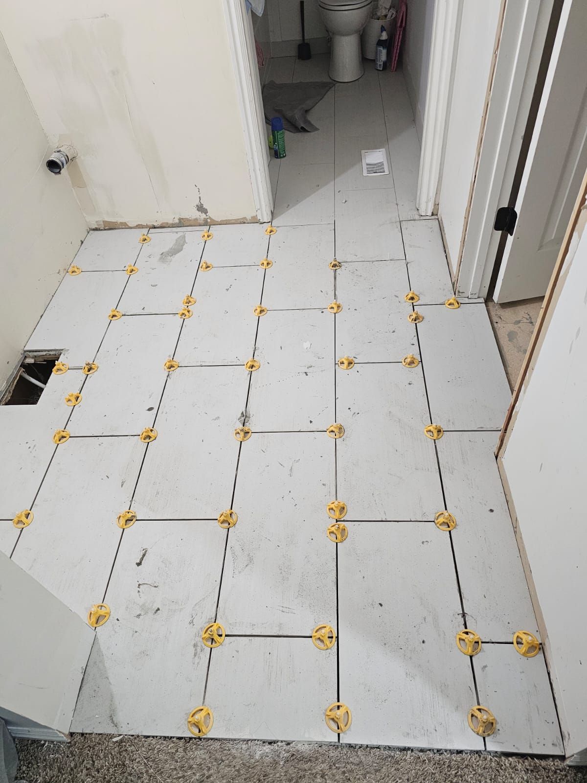 A bathroom floor is being tiled with white tiles and yellow spacers.