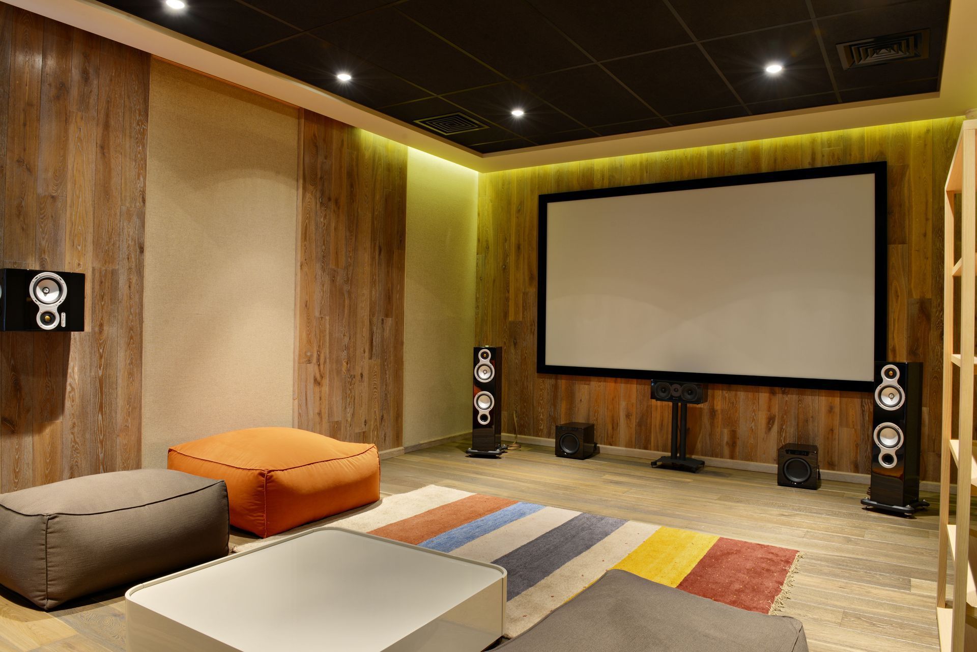 Modern home theater with large projection screen, speakers, and colorful seating on a wood-paneled wall backdrop