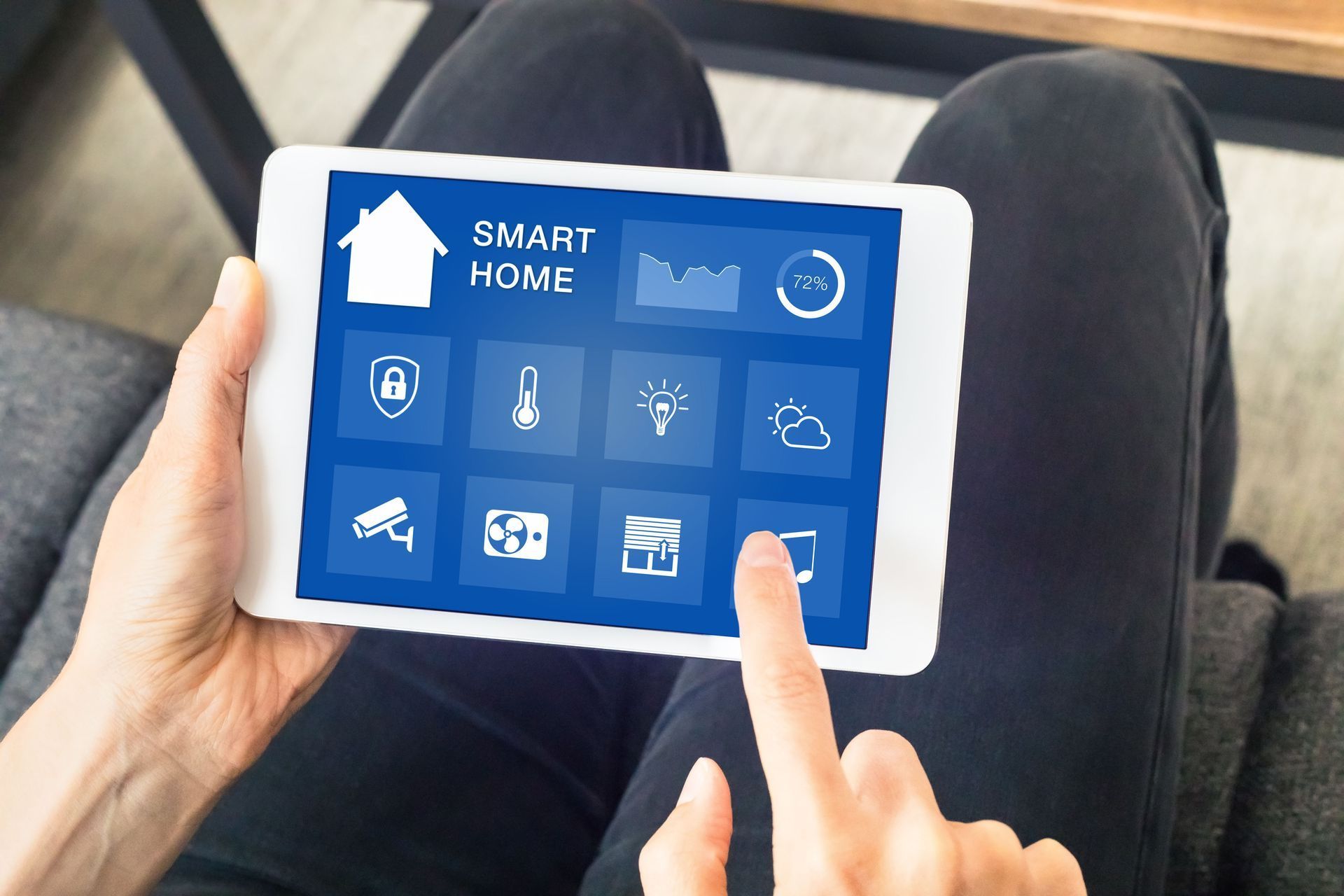 Hands holding a tablet showing a blue smart home control dashboard indoors