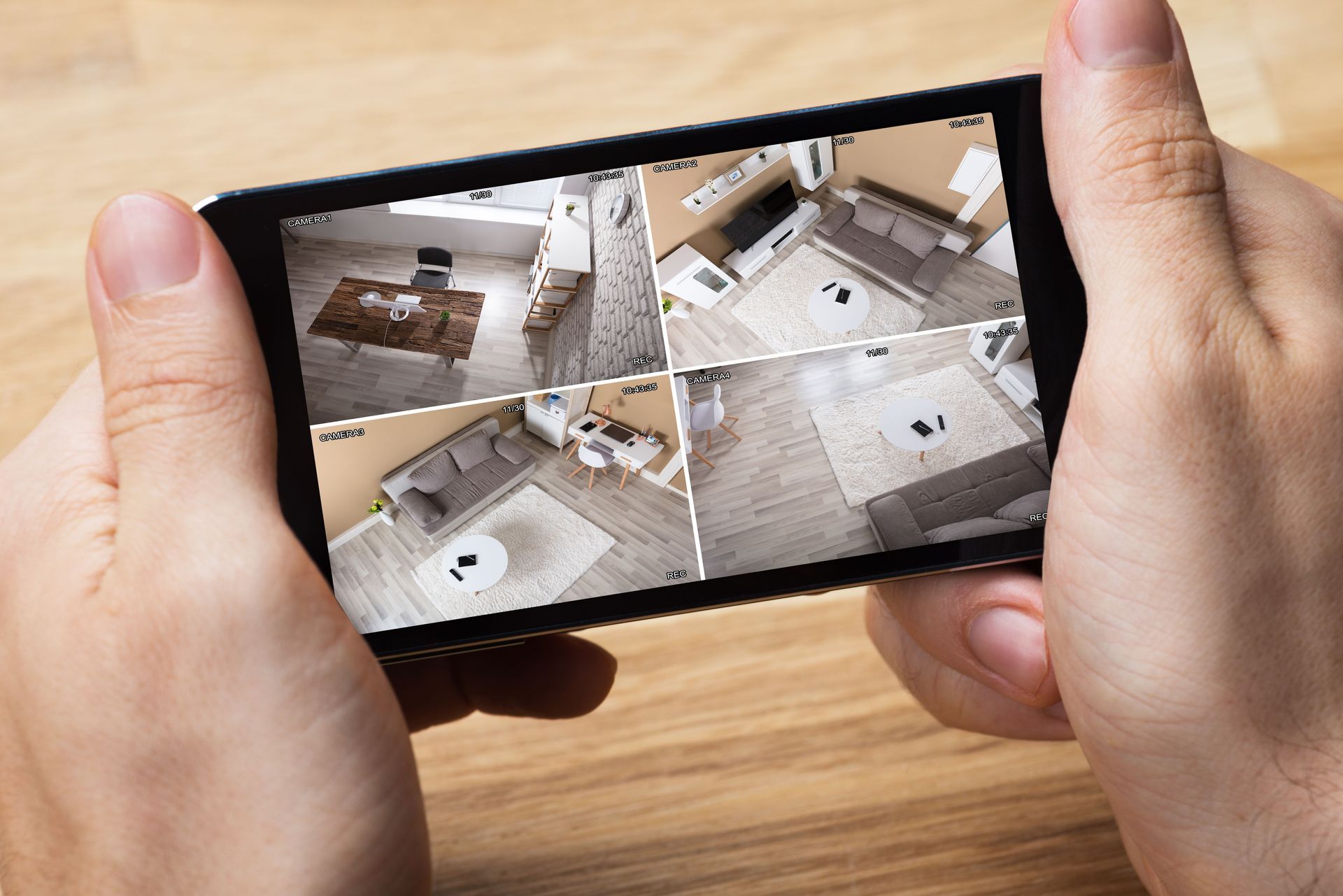 Hands holding a smartphone showing four security camera views of an empty room
