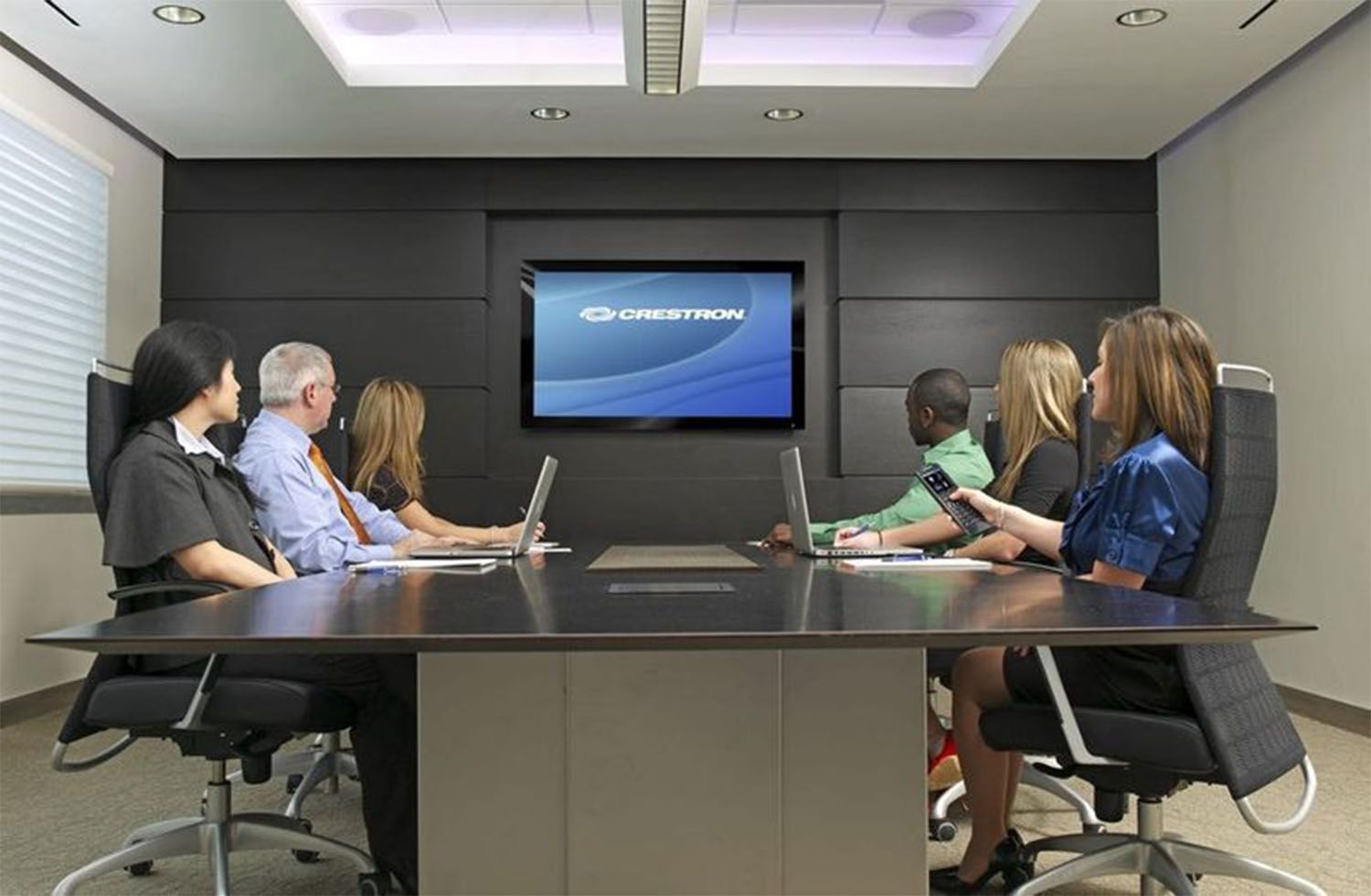 People in a conference room watching a presentation on a wall-mounted screen