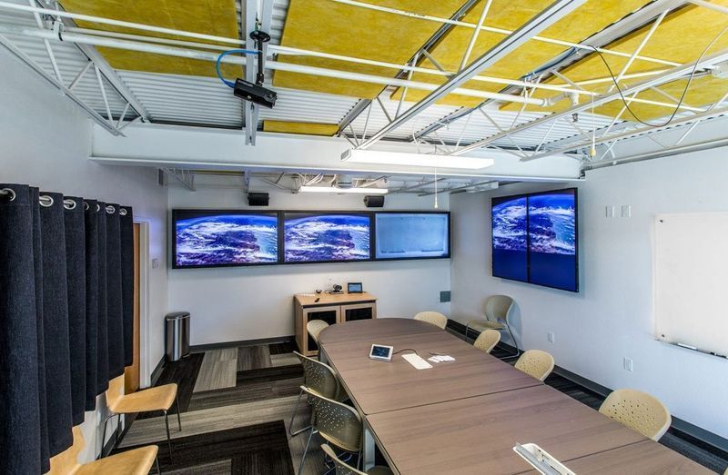 Conference room with long table, chairs, wall monitors, and exposed ceiling beams