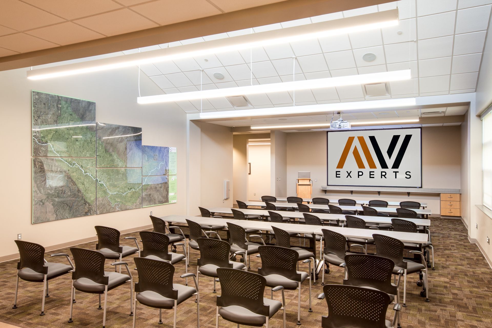 Conference room with rows of black chairs facing a presentation screen and AV Experts banner.