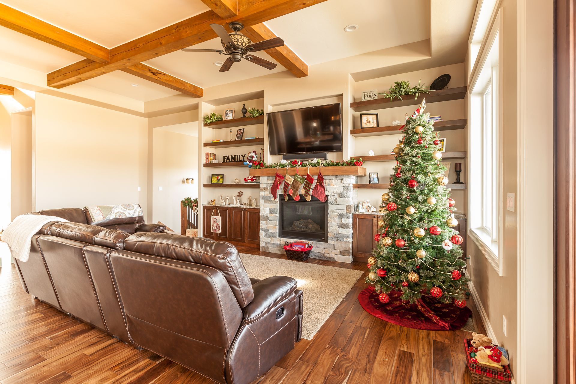 Cozy living room with stone fireplace, leather sofa, wooden beams, and decorated Christmas tree