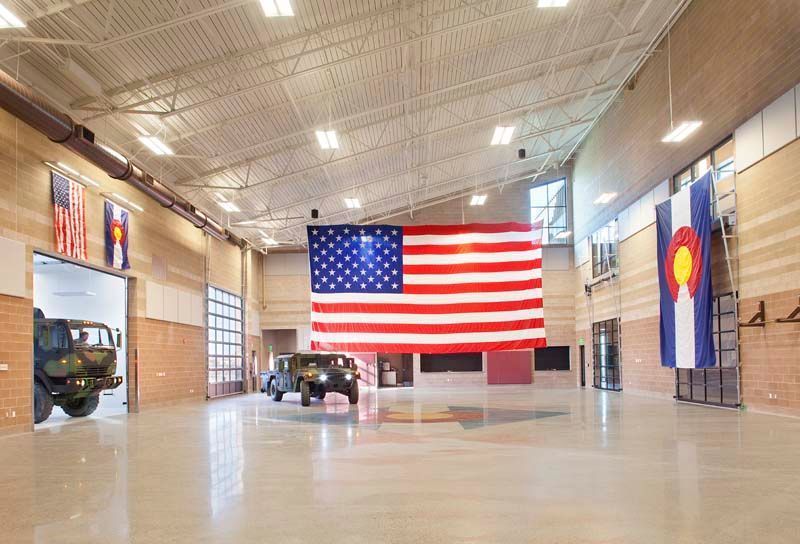 Large garage with a hanging U.S. flag and Colorado flag, vehicles parked inside, bright tiled floor