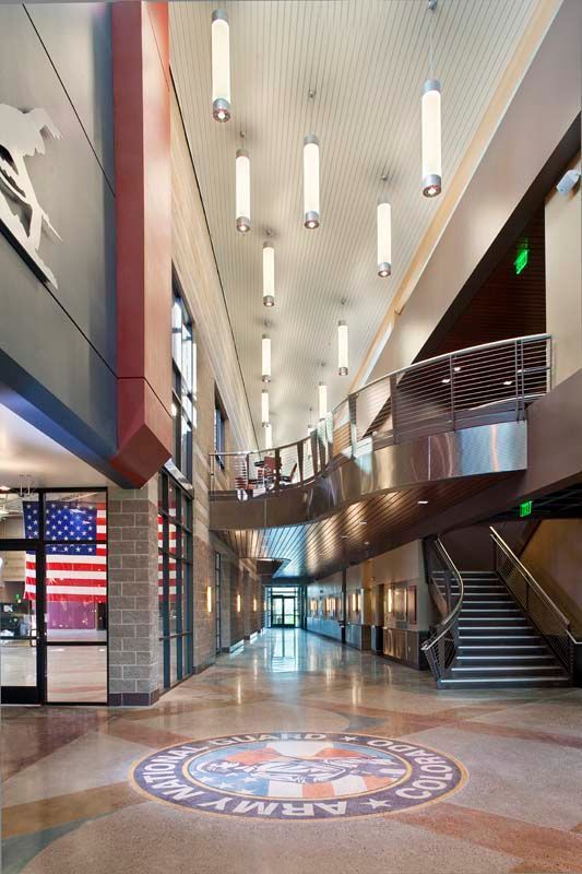 Modern atrium interior with tall hanging lights, staircase, glass railings, and large American flag display.