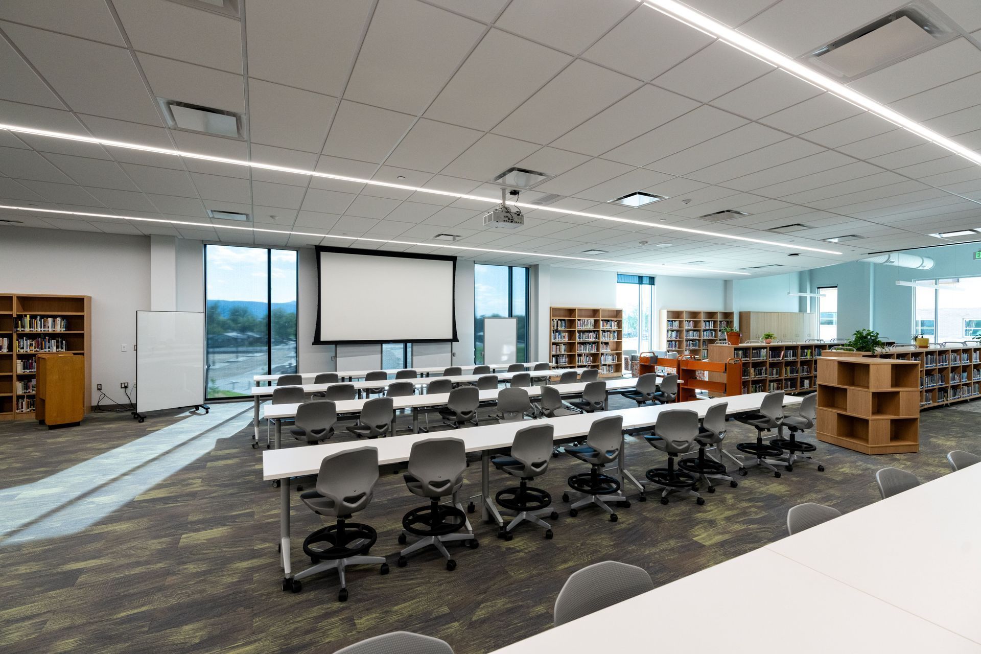 Empty modern classroom with rows of chairs, tables, projector screen, and bookshelves