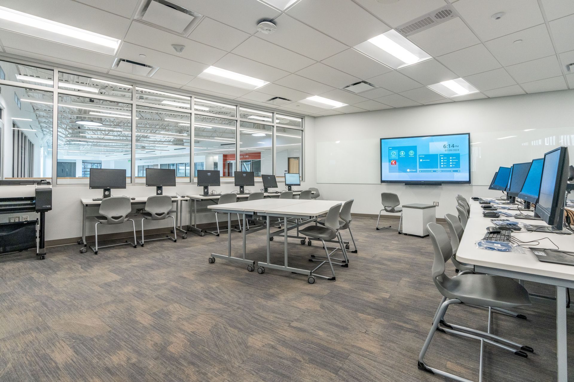 Modern computer lab with rows of desks, monitors, and a large display screen in a bright office-like room