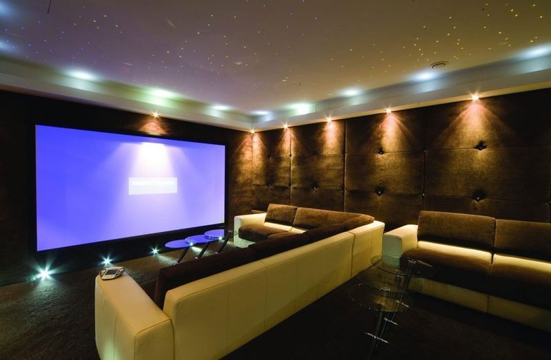 Luxury home theater with a large glowing screen, sofas, and dark wood-paneled walls