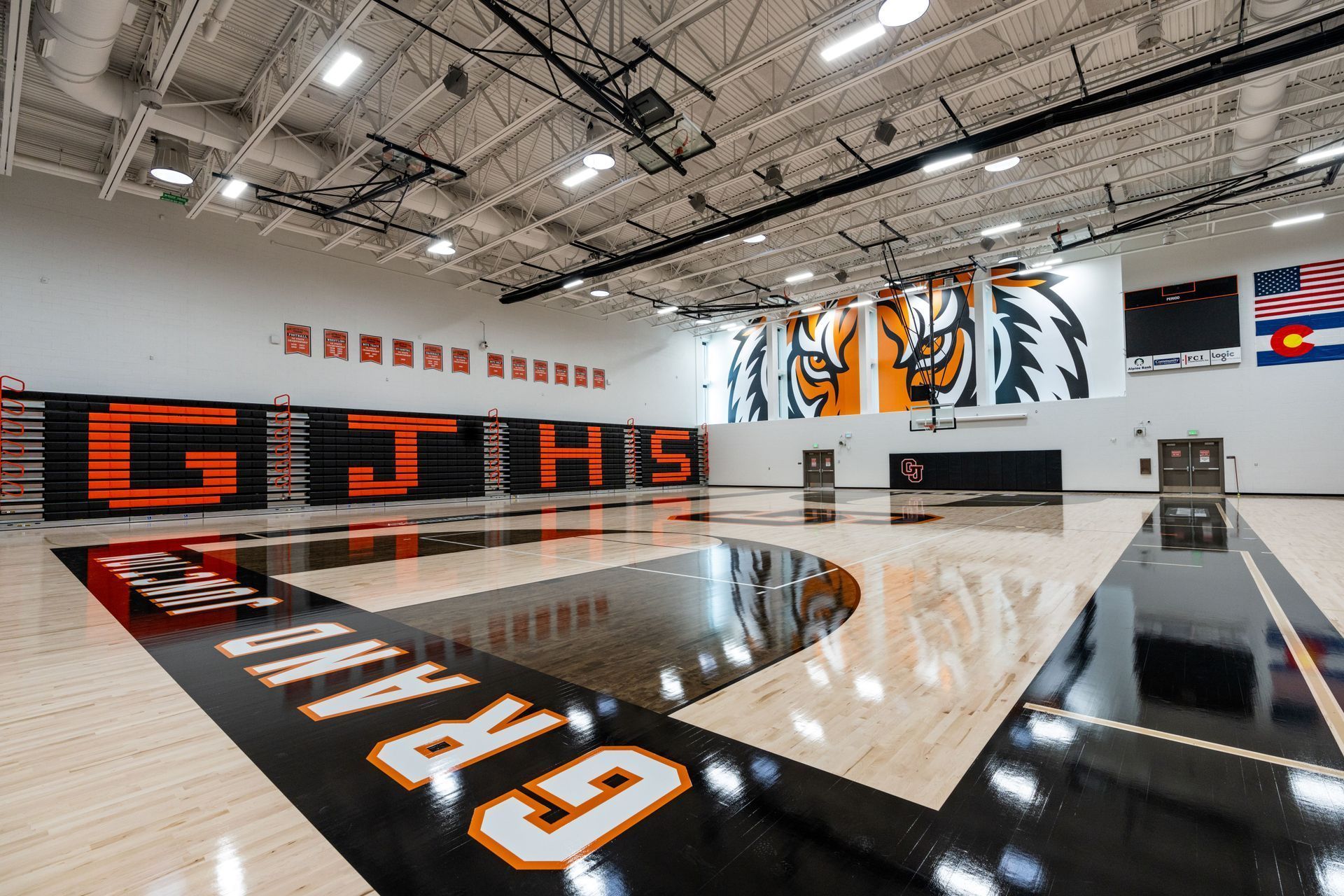 Indoor high school gym with glossy court, black-and-orange tiger mural, and “Grit” lettering on the floor