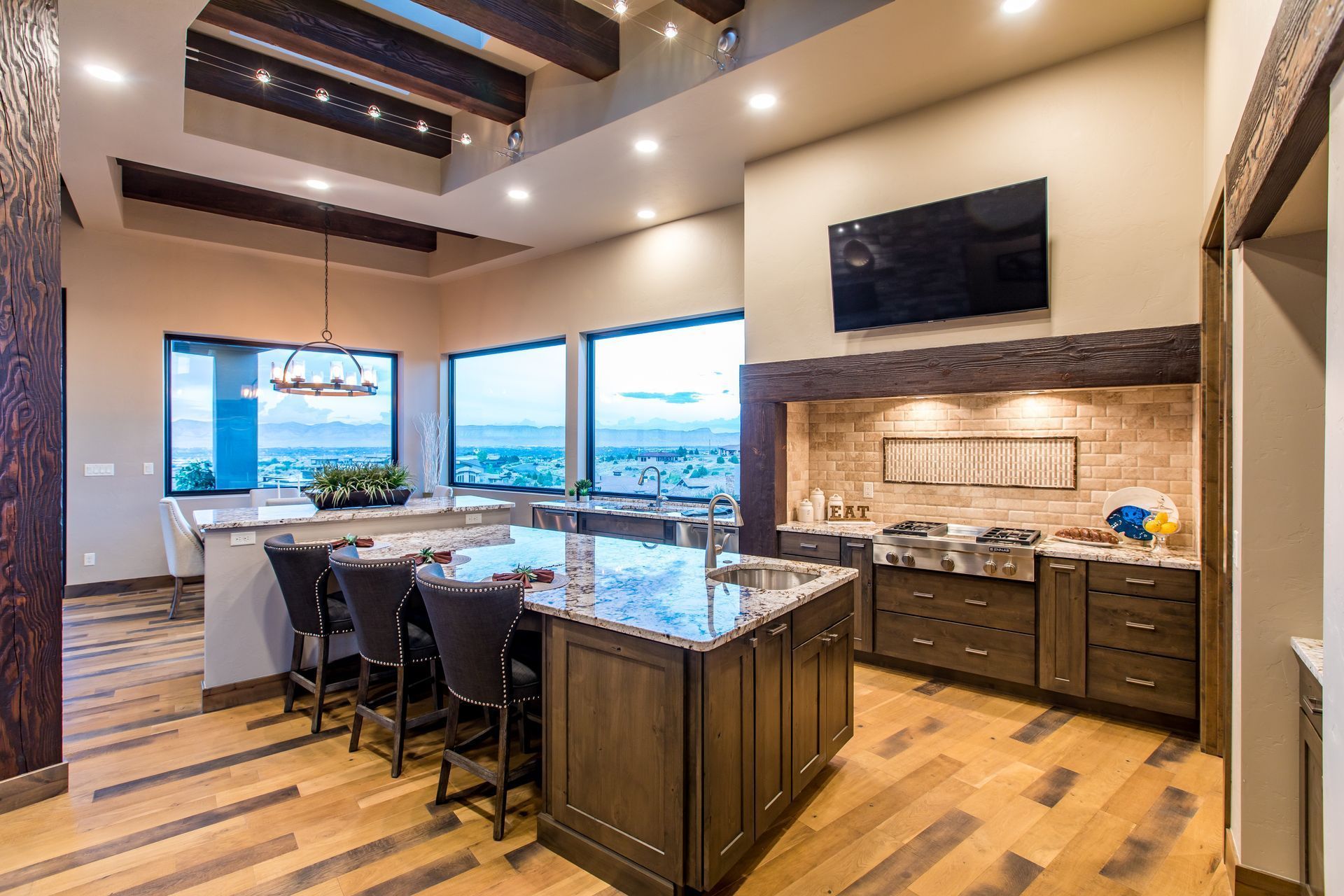 Modern kitchen with large island, bar stools, wood beams, and a built-in grill area by big windows