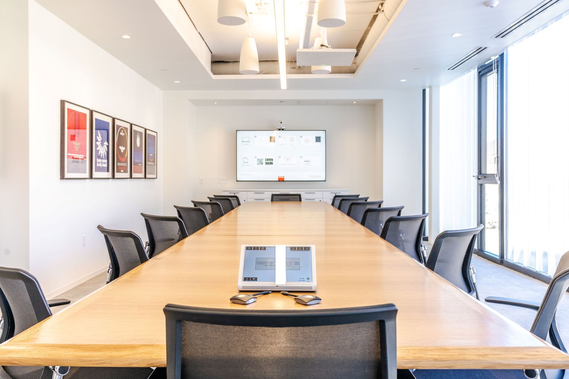 Modern conference room with a long wooden table, black chairs, and a wall-mounted presentation screen
