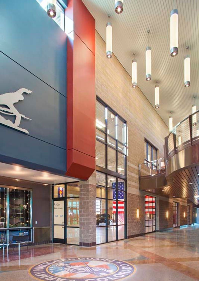 Modern lobby with tall tan walls, red accents, hanging lights, and a polished floor with a circular emblem.