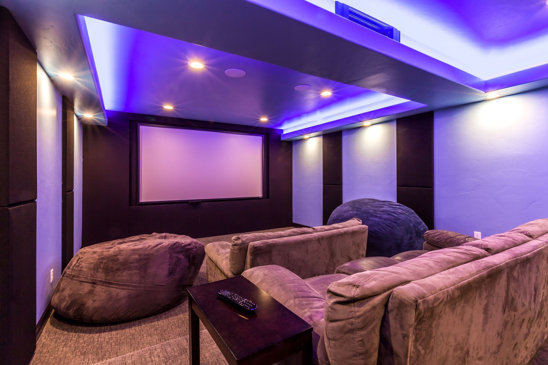Purple-lit home theater with plush sectional seating and a large projection screen