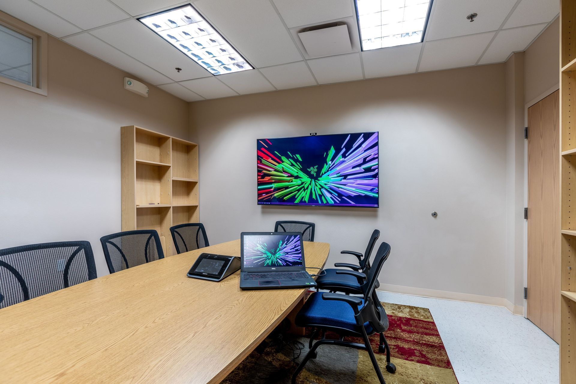 Conference room with a long table, chairs, laptop, and wall-mounted colorful display.