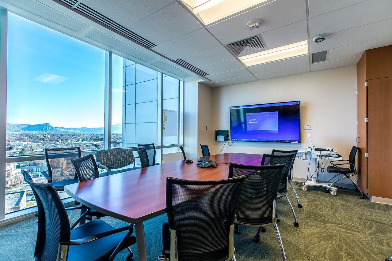 Modern conference room with a long table, black chairs, wall-mounted TV, and city view through large windows