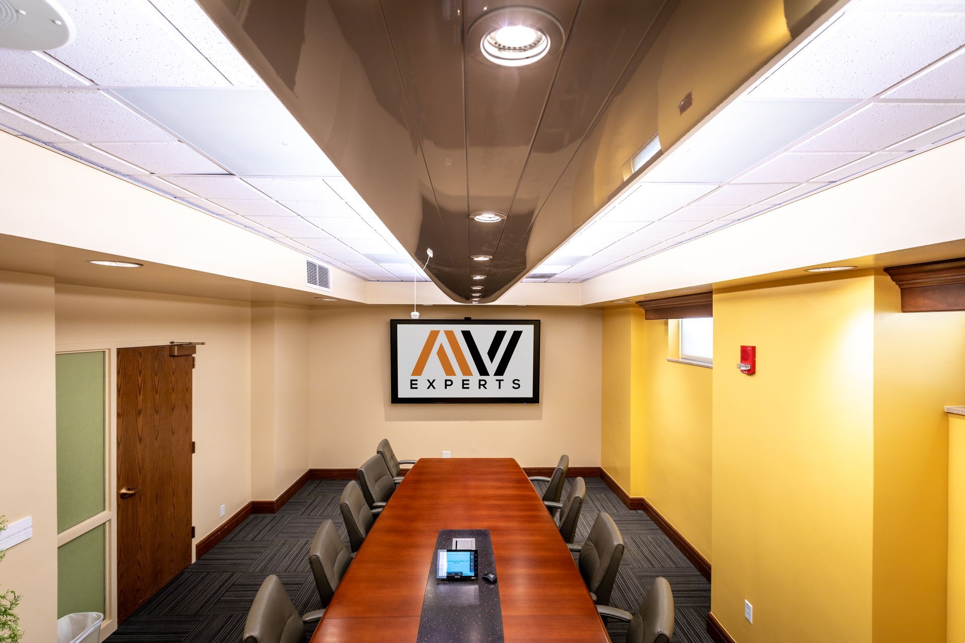 Empty conference room with long table, striped chairs, and a wall-mounted TV at the far end.