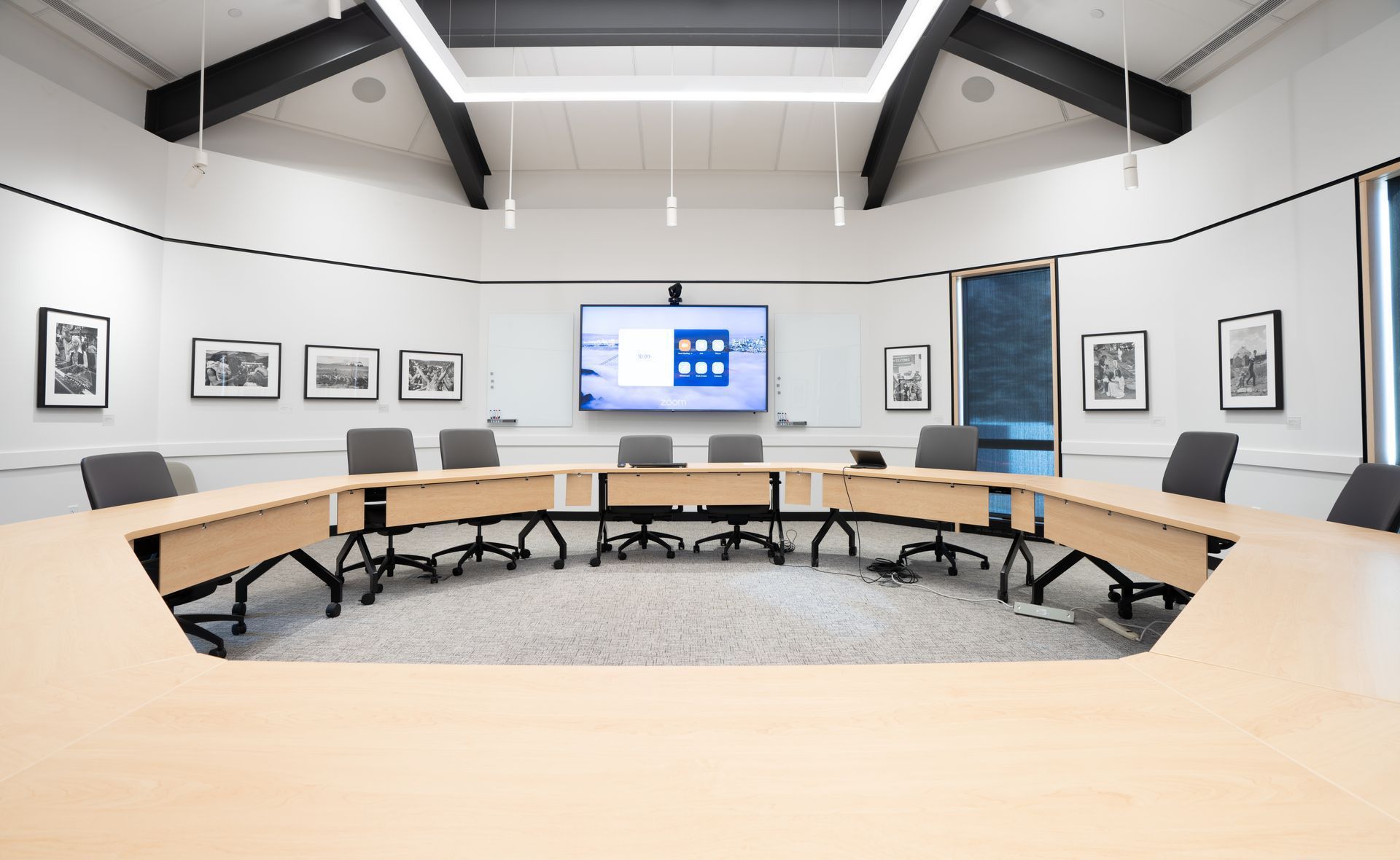 Modern conference room with curved tables, gray chairs, wall art, and a central presentation screen