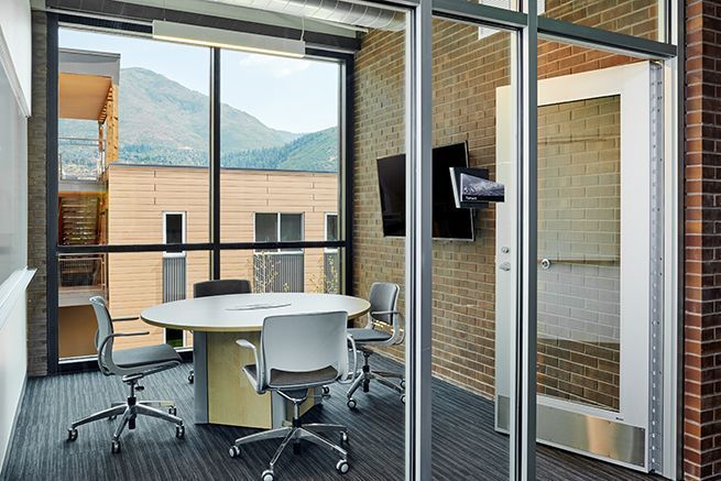 Modern glass-walled meeting room with round table, swivel chairs, and mountain view outside