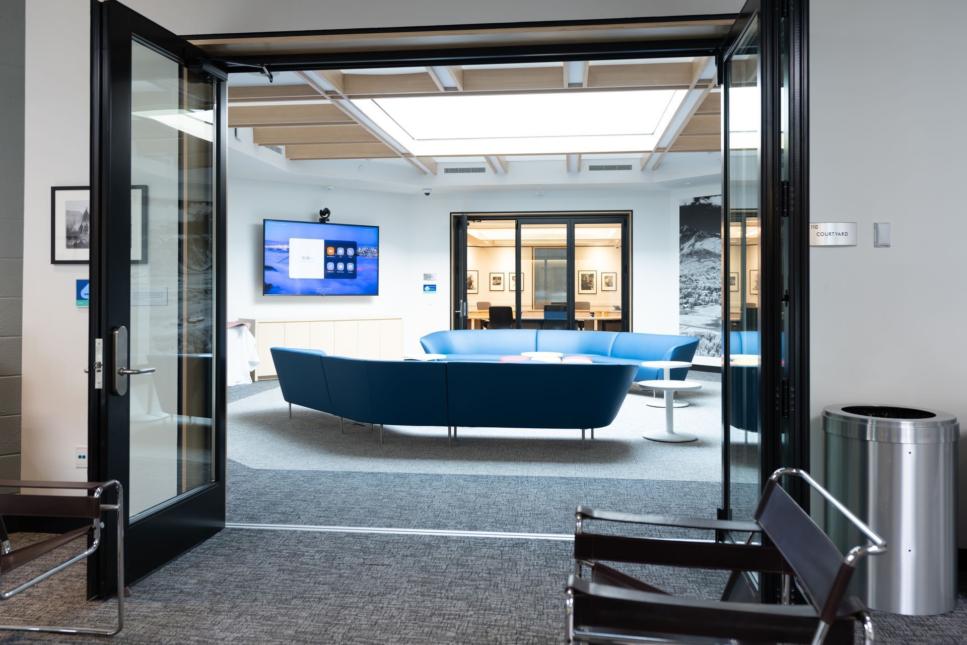 Modern office lounge with blue sofas, glass doors, and a wall-mounted screen