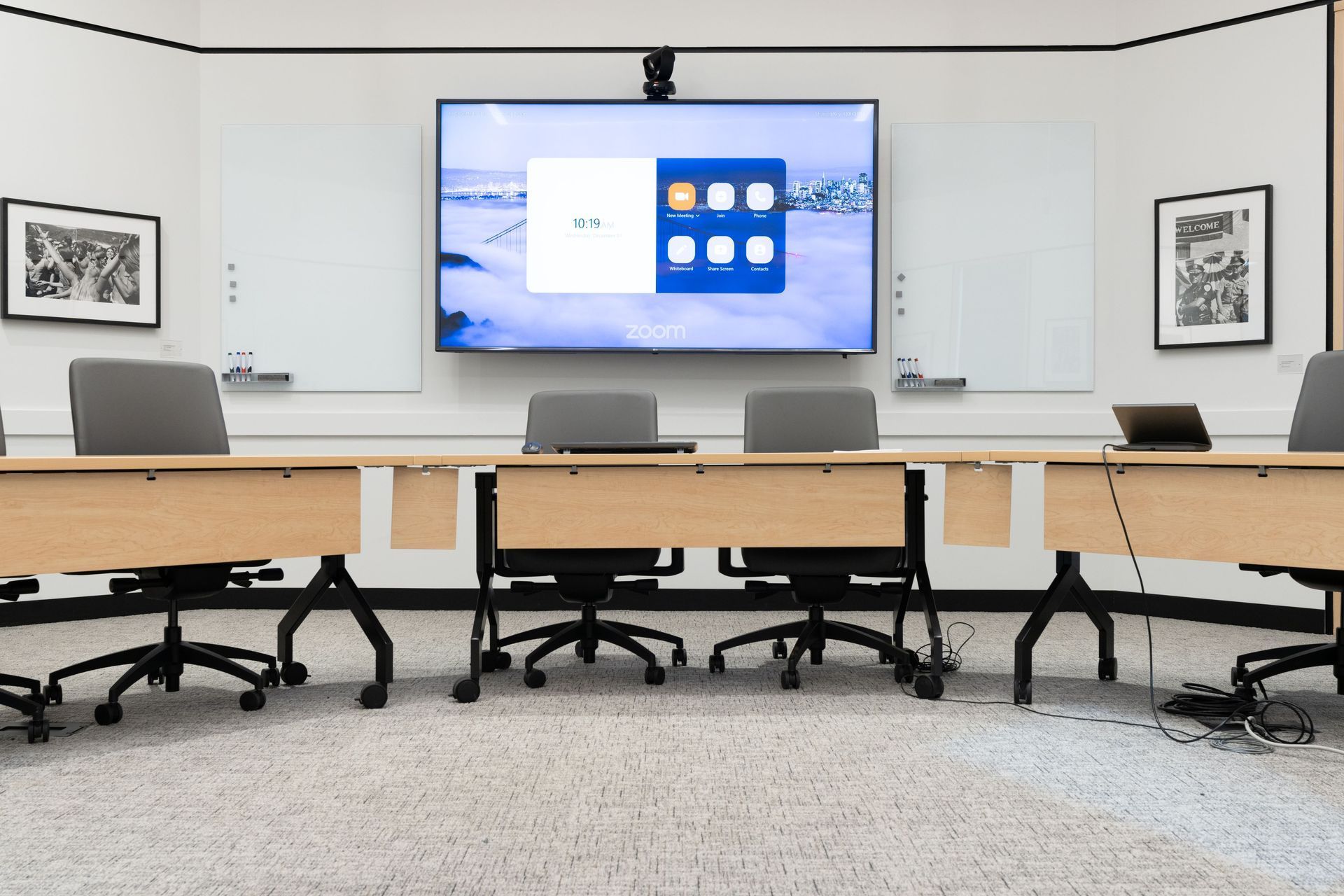 Modern conference room with large wall display, whiteboard, and wood meeting tables with chairs