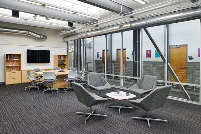 Modern office lounge with chairs, desks, glass walls, and a small meeting table