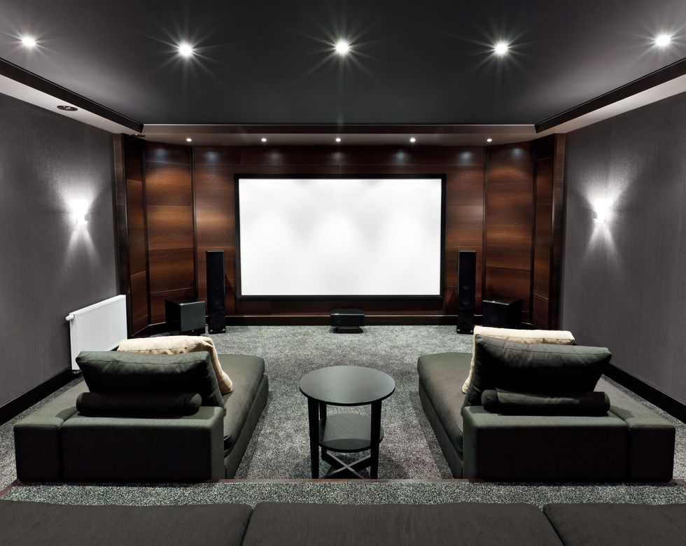 Home theater room with two dark sofas, round table, and large projection screen