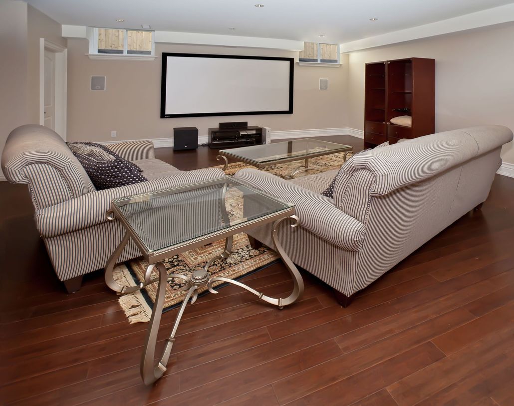 Home theater room with striped sofas, glass coffee table, projector screen, and hardwood floor