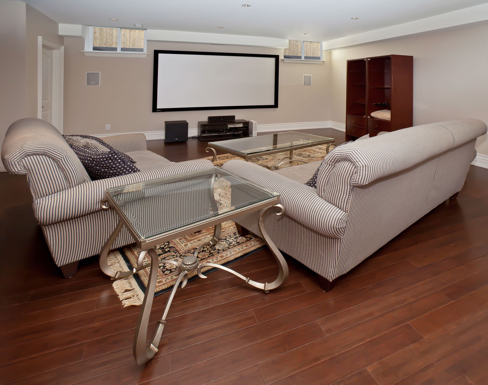 Modern living room with striped sofas, glass coffee table, projector screen, and hardwood floors