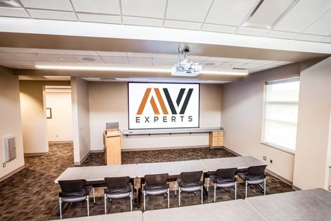 Conference room with AV Experts logo on the front wall, long table, chairs, and projector screen on the ceiling