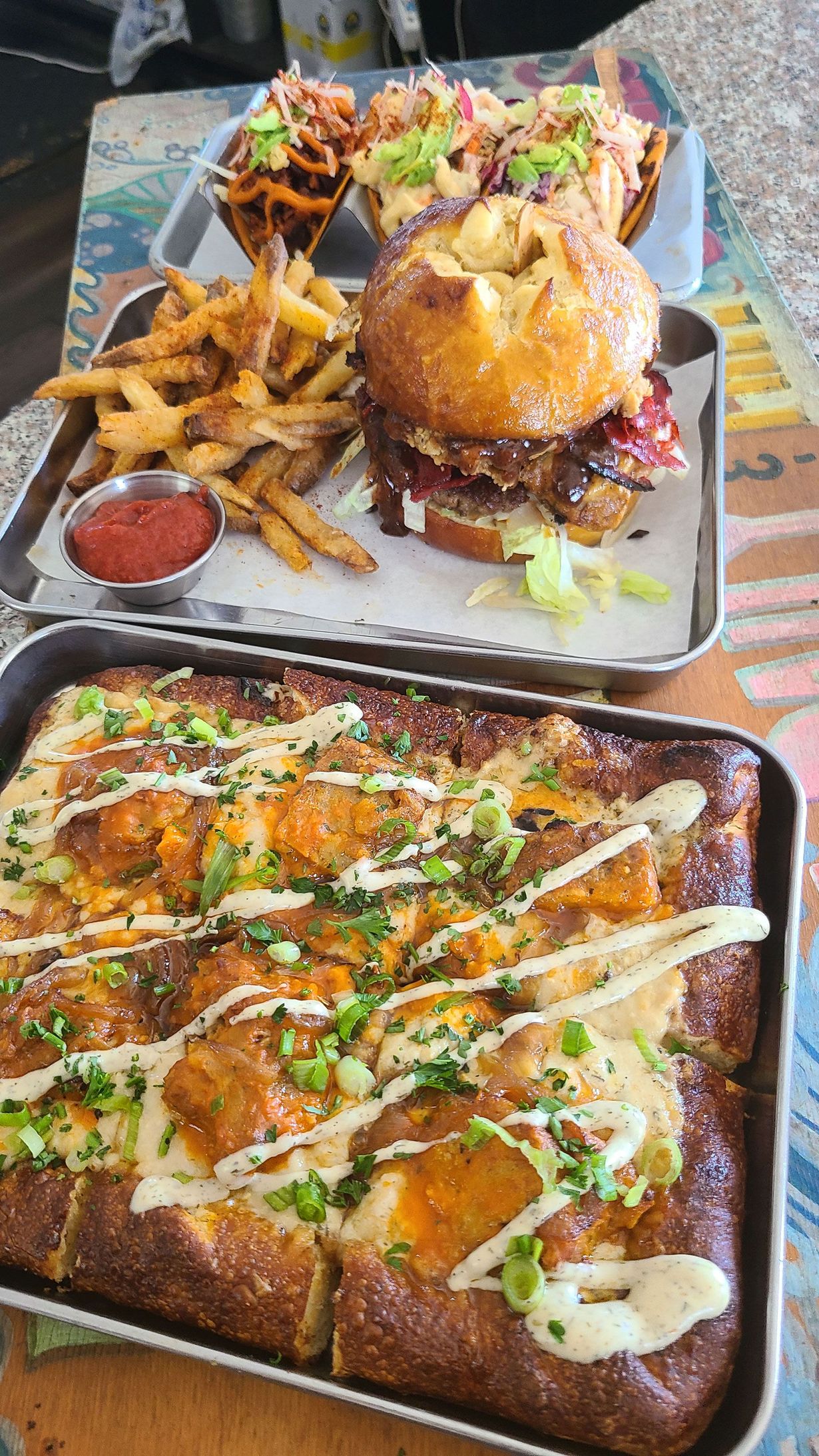 Tray of food: burger, fries, tacos, and square pizza with toppings.