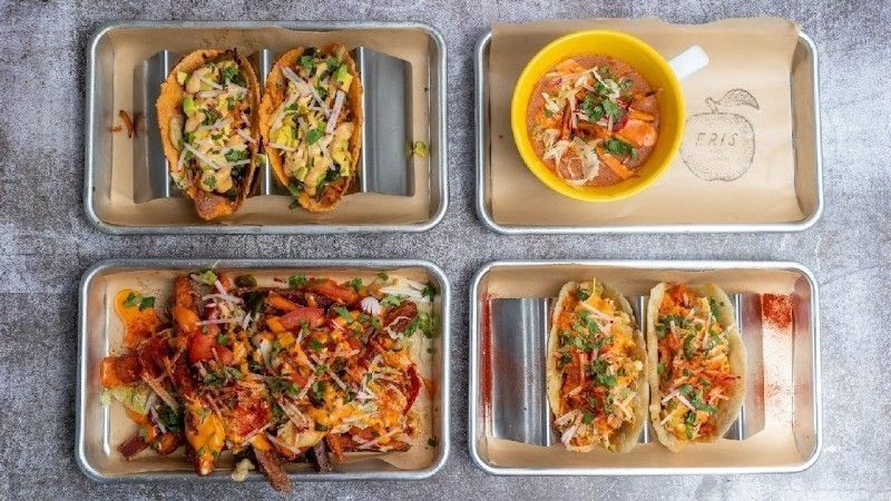Four metal trays of food: tacos and soup, on a mottled gray surface.