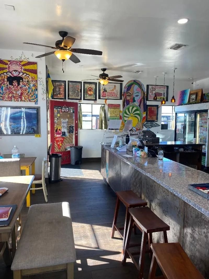 Interior of a colorful cafe with art on the walls, a counter with stools, and tables.