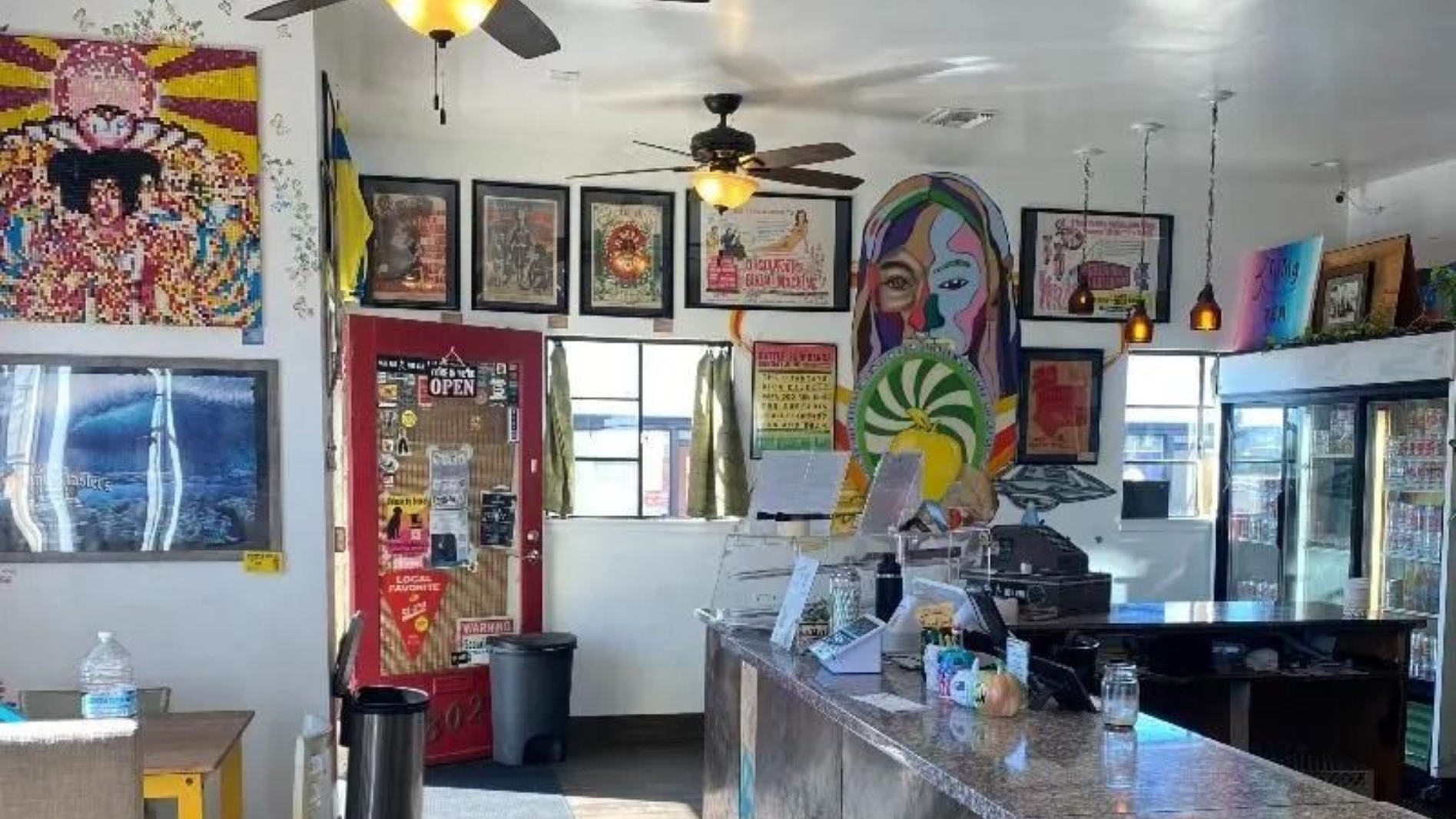 Narrow alleyway with blue murals, wooden structures, and a tent with tables under a clear blue sky.
