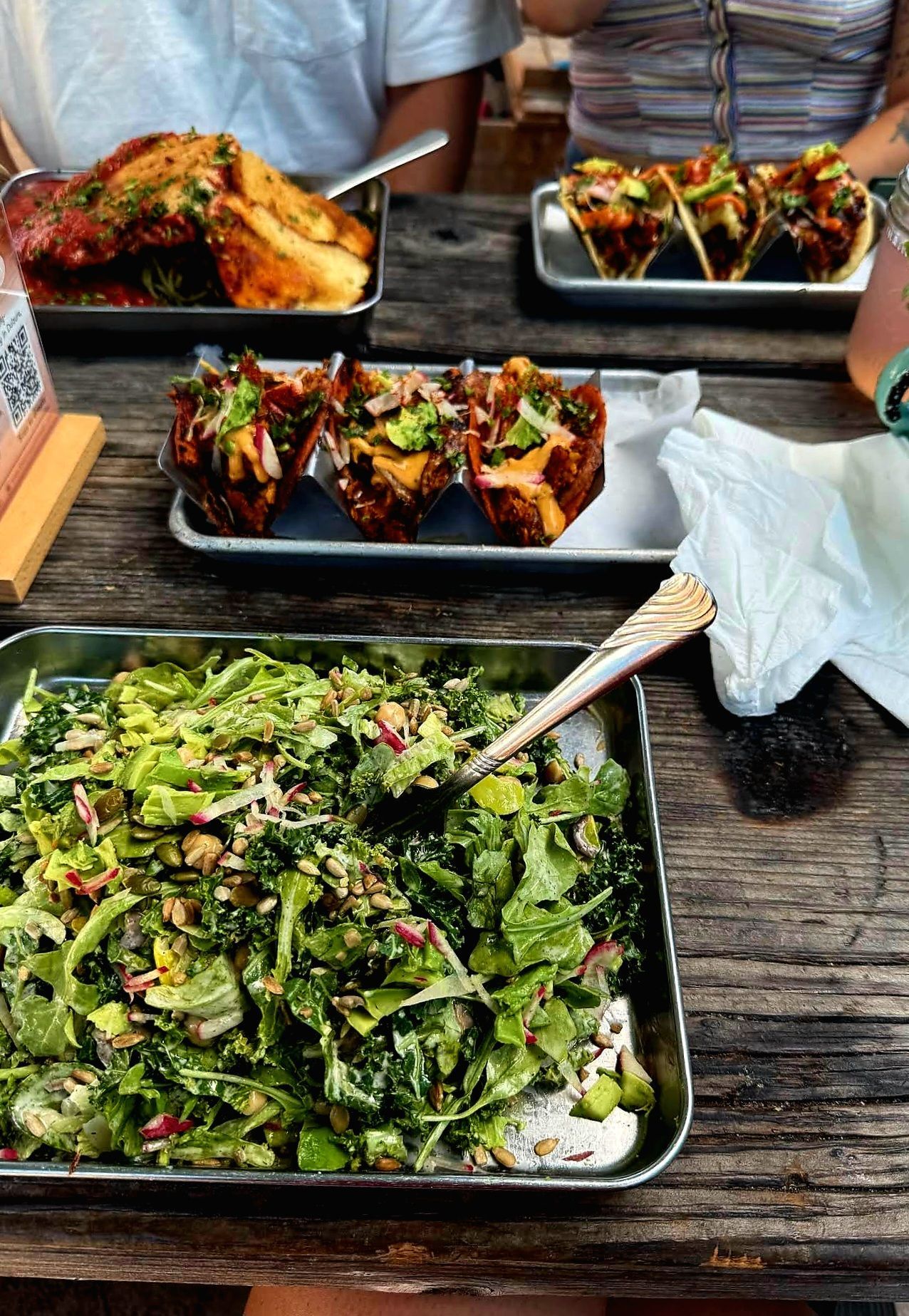 A table spread of food: salad, tacos, and a meat dish. Two people are visible at the table.