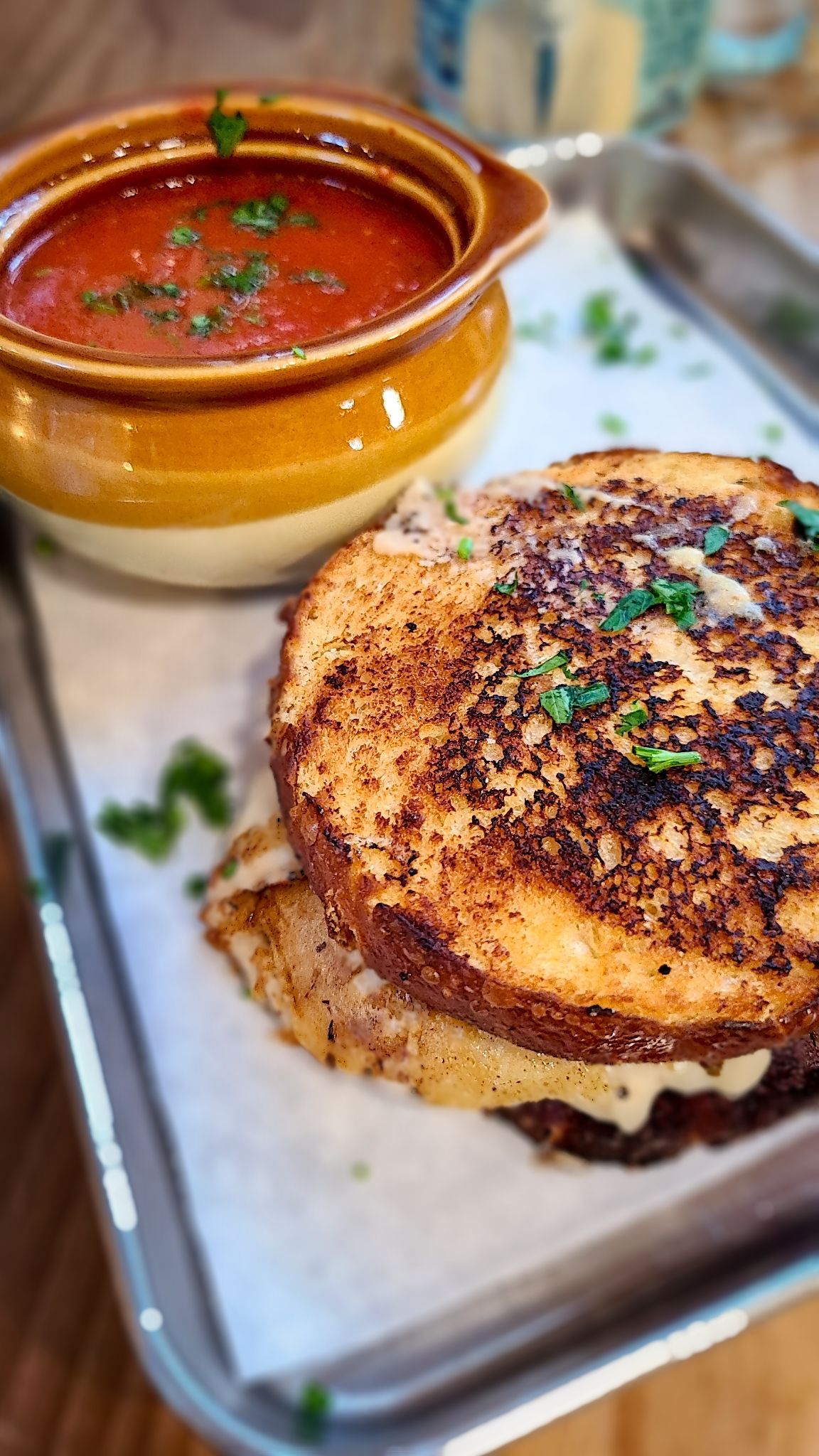 Grilled cheese sandwich with tomato soup, garnished with parsley on a tray.