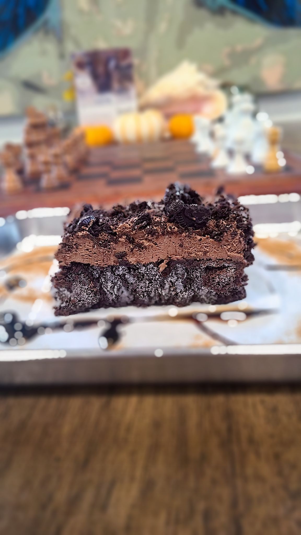 Chocolate cake slice on a plate, with chocolate frosting. Wooden table background.
