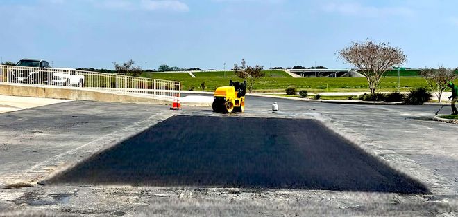 A compact yellow roller compacting fresh asphalt in a parking lot.