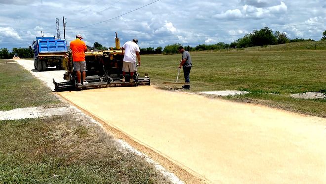 Road construction: Workers laying asphalt with a paving machine on a sunny day.