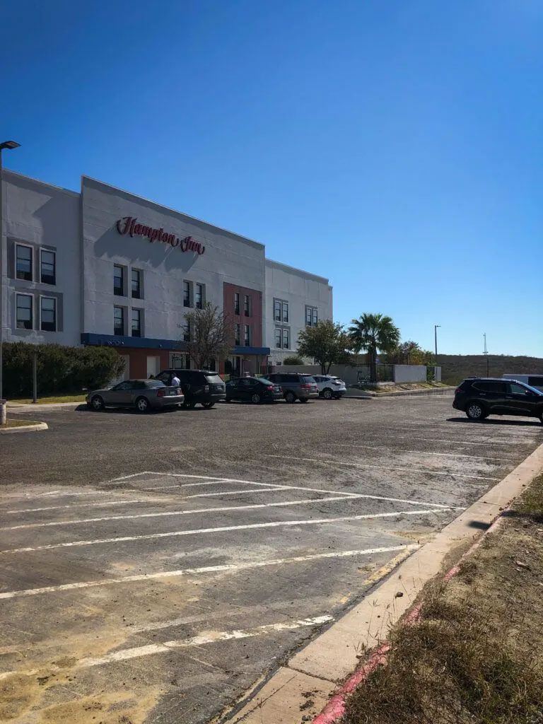 Hampton Inn hotel building with parked cars in front on a clear, sunny day.