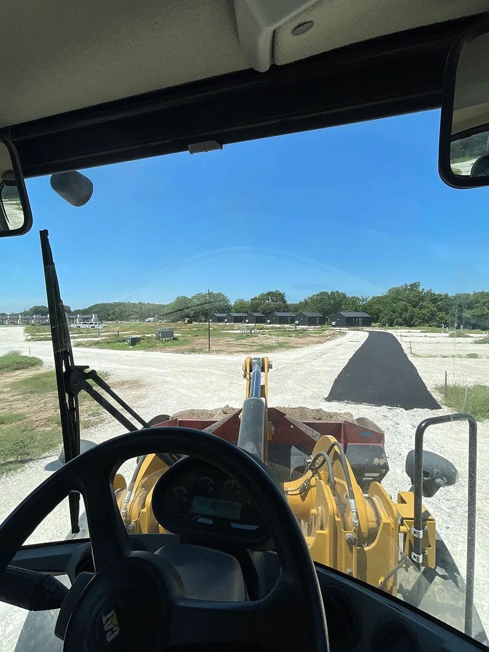 View from inside a yellow construction vehicle. Bright blue sky. Vehicle approaching a gravel pile and crossroads.