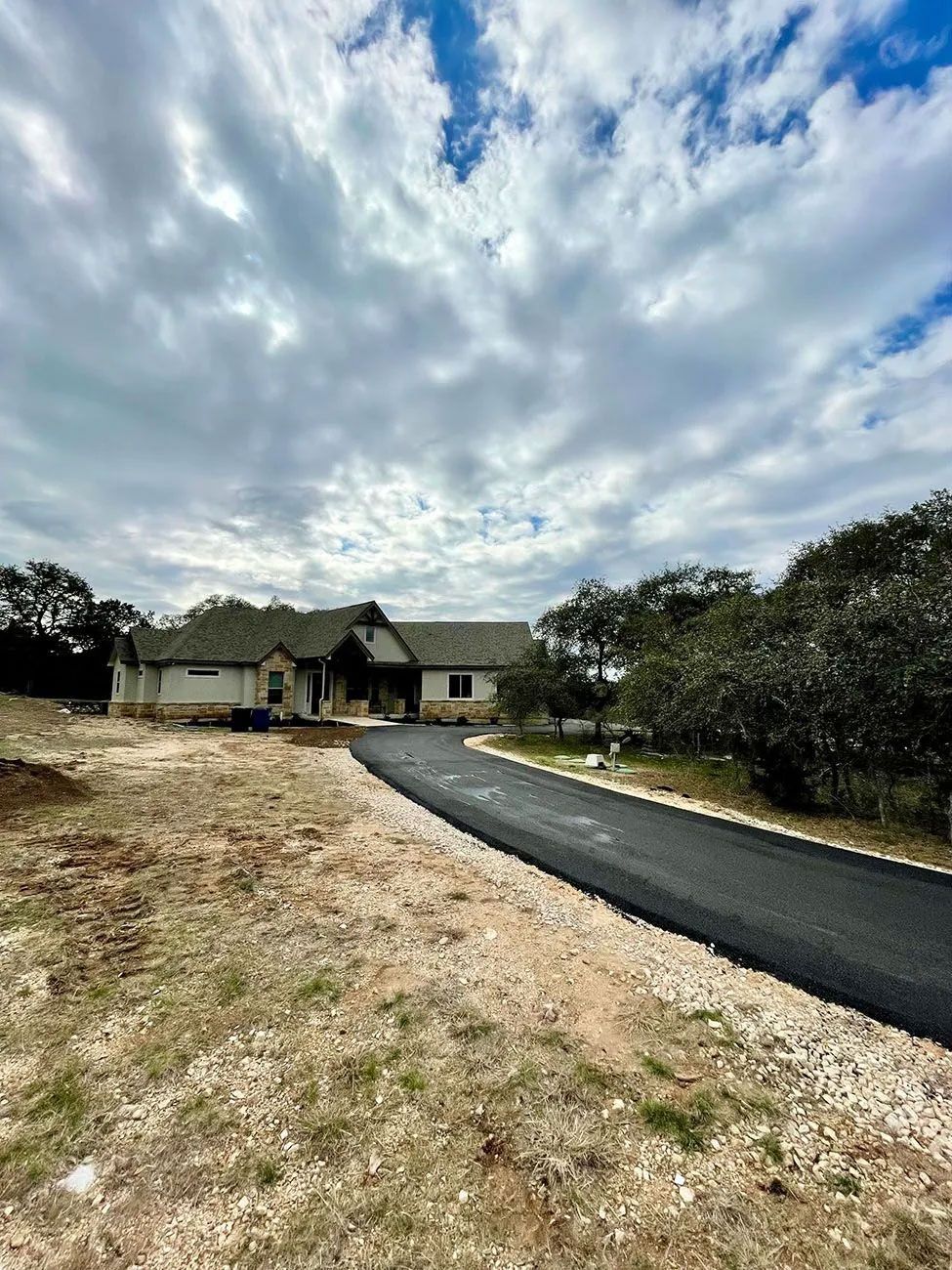 A house with a black asphalt driveway under a cloudy sky.