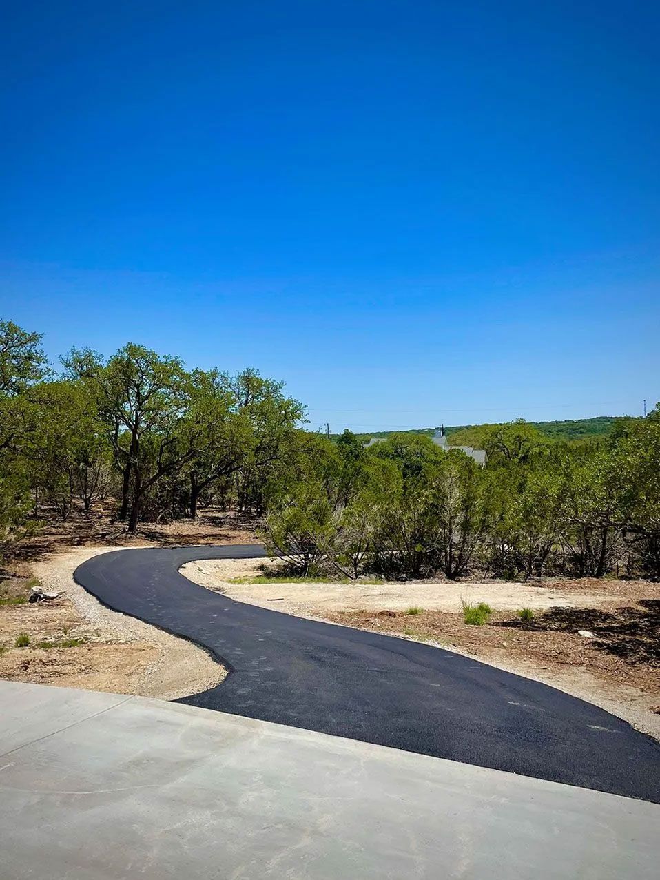 Paved road curves through a wooded area under a clear blue sky.