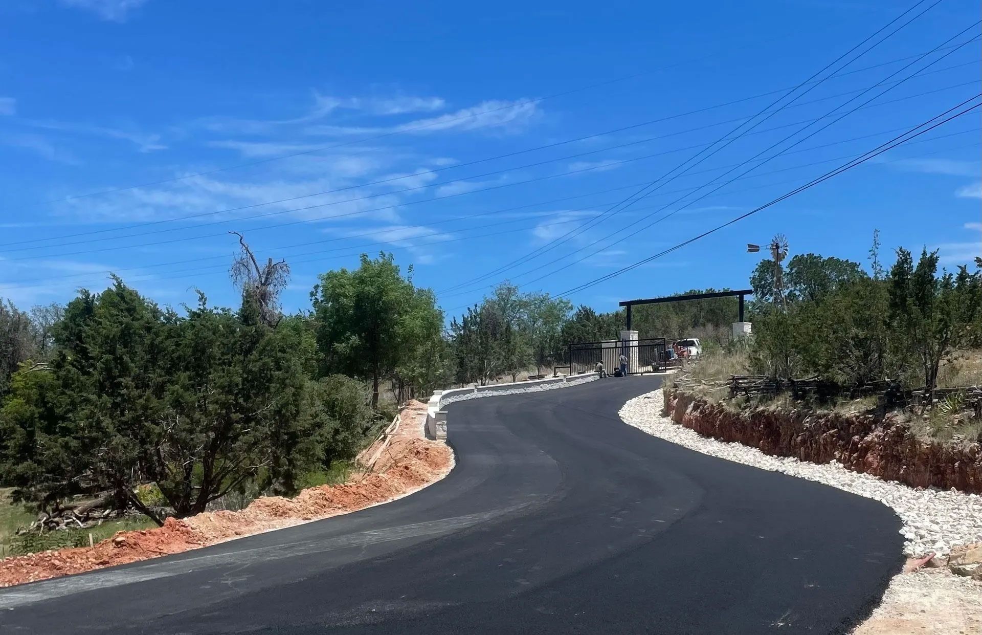 Paved road winding through a landscape with trees and a blue sky. Gravel borders the road.