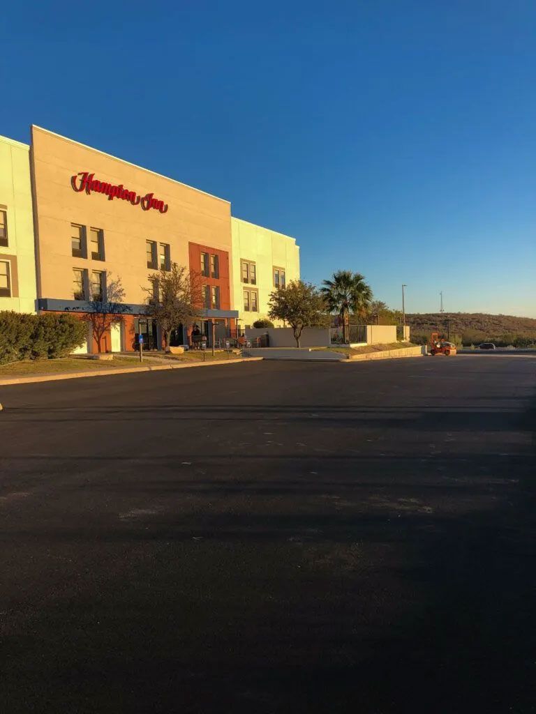Hampton Inn hotel building under a clear blue sky. Beige and red facade, empty parking lot.